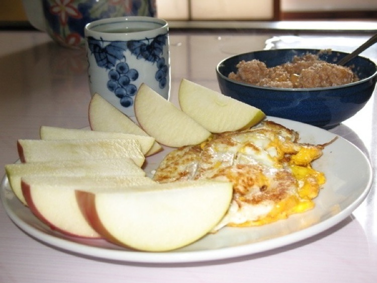 A picture of a breakfast course with an apple, eggs, oatmeal and a cup of tea.